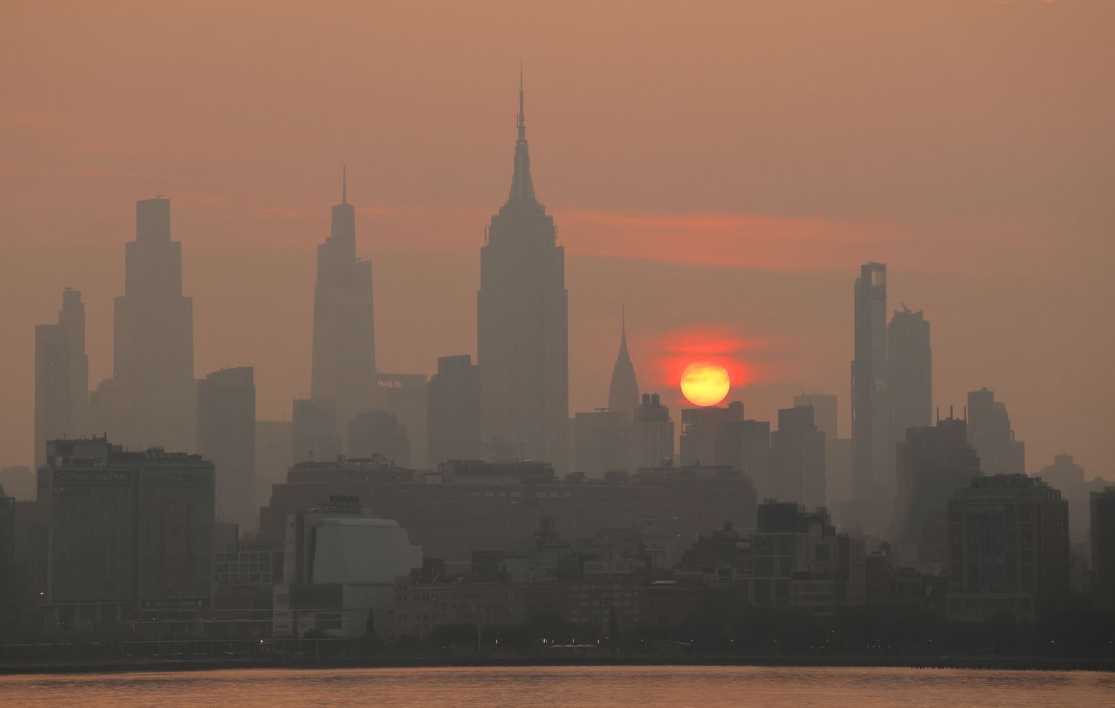 A city skyline obscured by thick orange-brown wildfire smoke