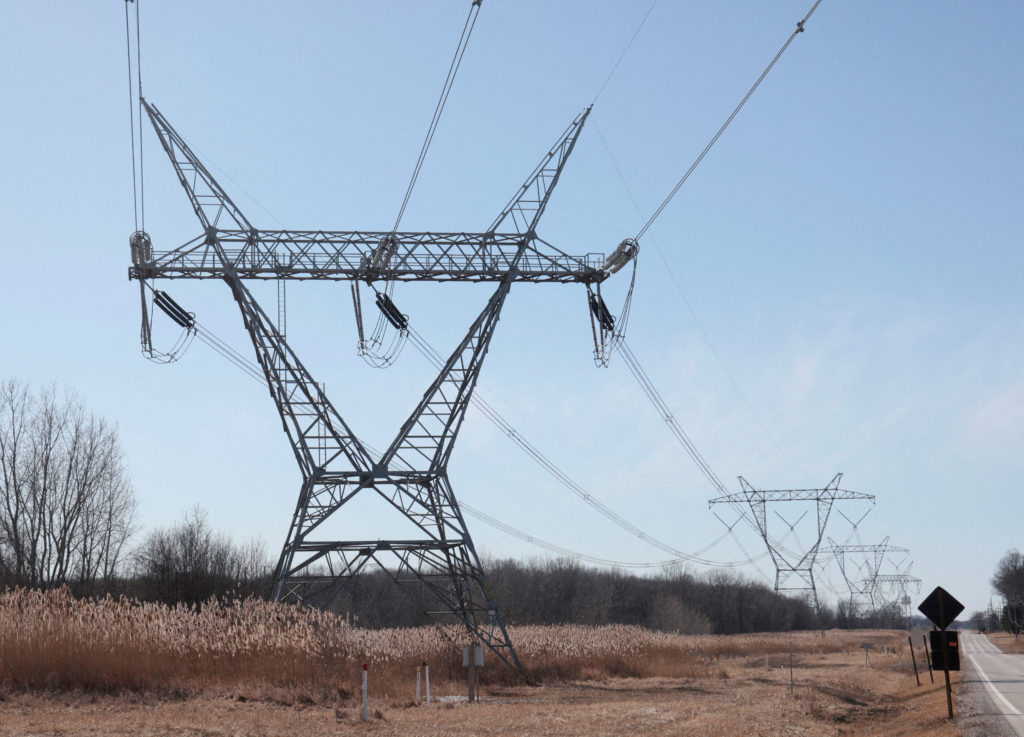 High-voltage transmission towers across rural farmland under a cloudy sky